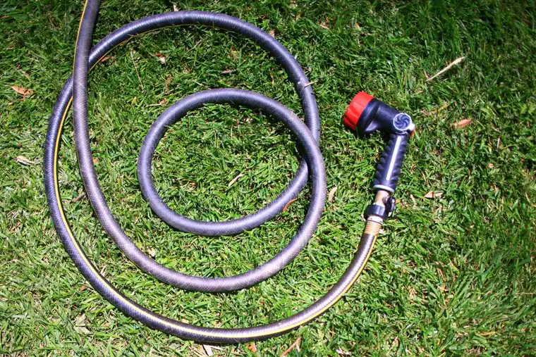 Dark rubber garden hose coiled loosely on grass with a spray gun attached