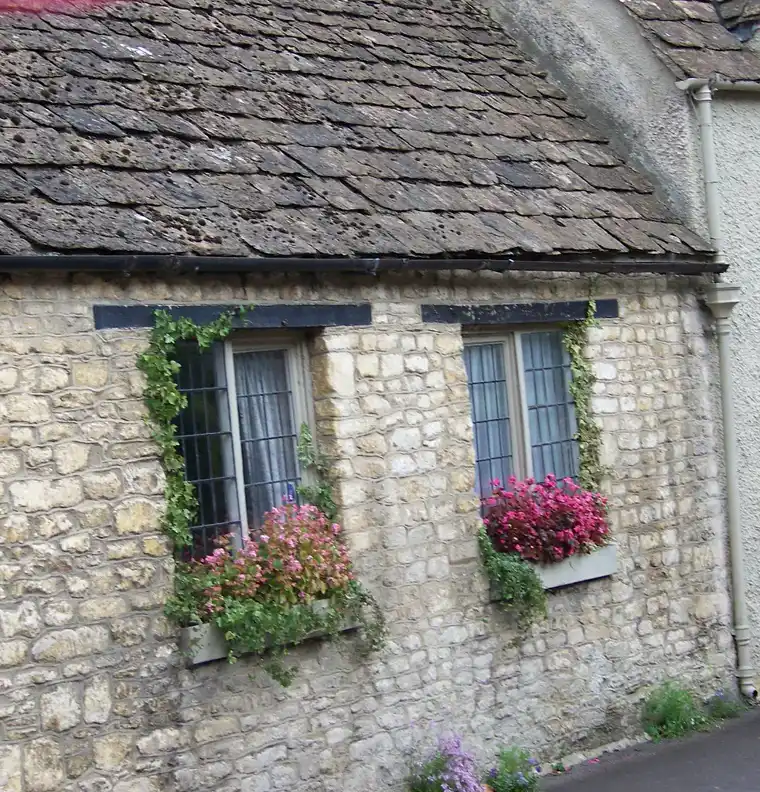 Stone cottage windows with geranium-filled window boxes