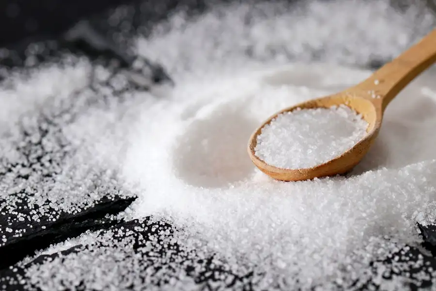 White mineral salt crystals heaped on a wooden spoon.