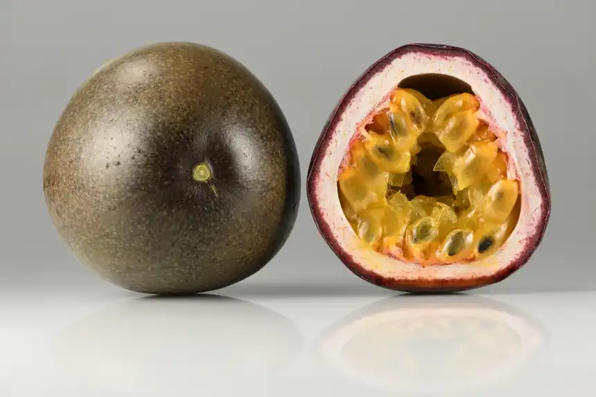 Whole purple passionfruit beside a halved one showing golden pulp and dark seeds