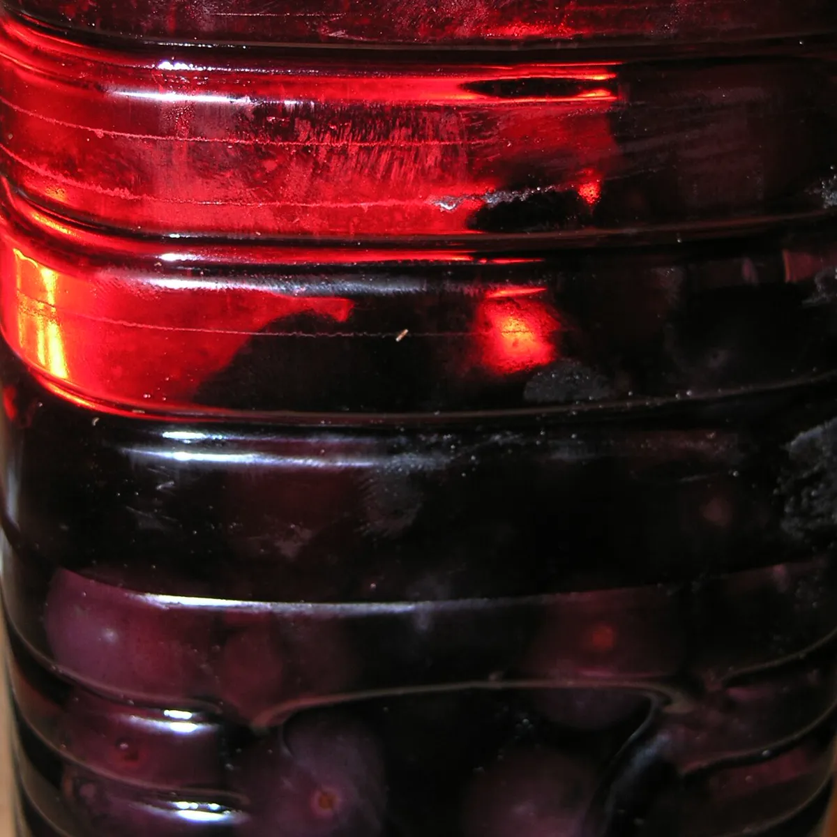 Whole damsons steeping in a sealed jar of gin, the fruit staining the liquid deep red