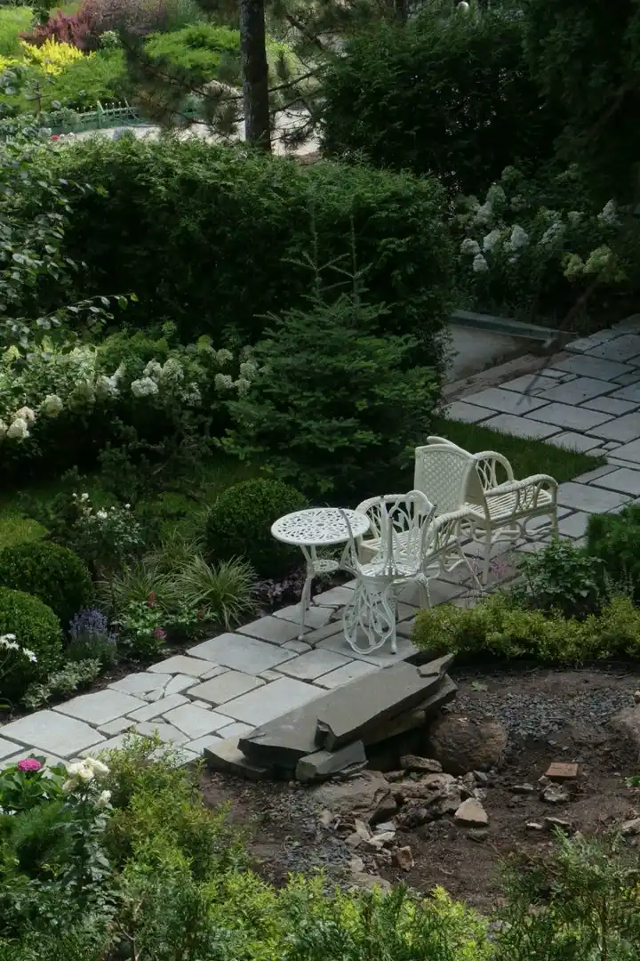Small garden seating nook with a white bistro set on a stone path among layered planting