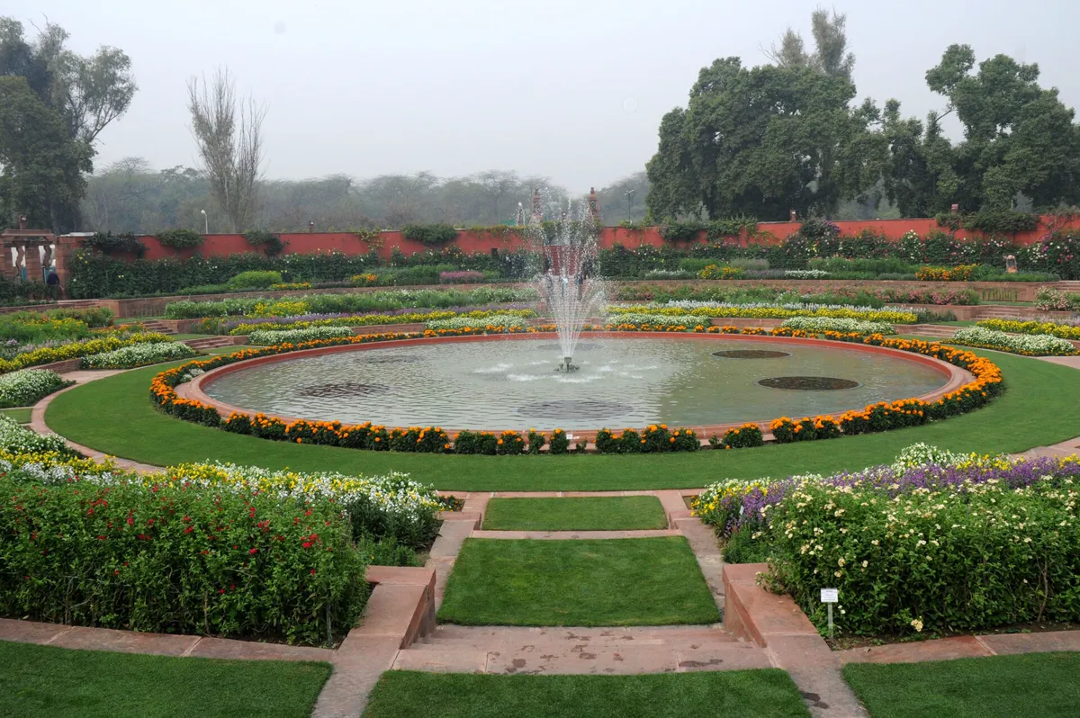 A circular sunken garden with a wide round pool and central fountain, ringed by marigolds and terraced flower beds