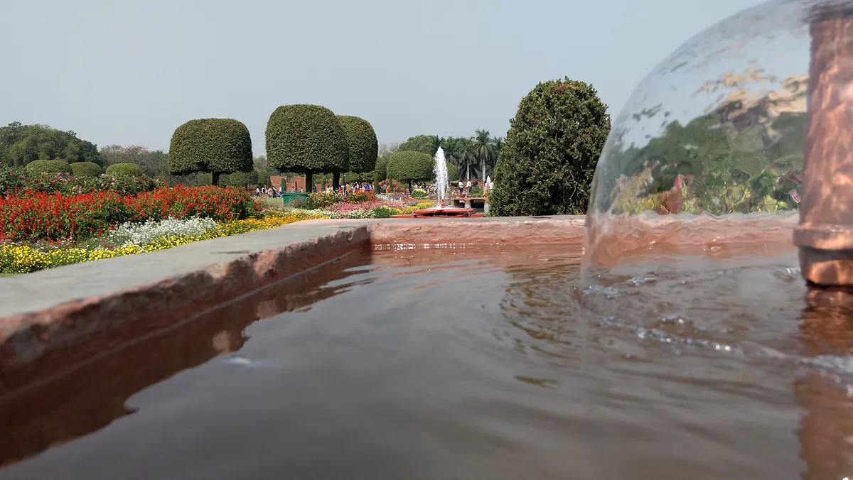 A narrow sandstone water channel photographed at water level, with a low jet in the foreground and flower borders beyond