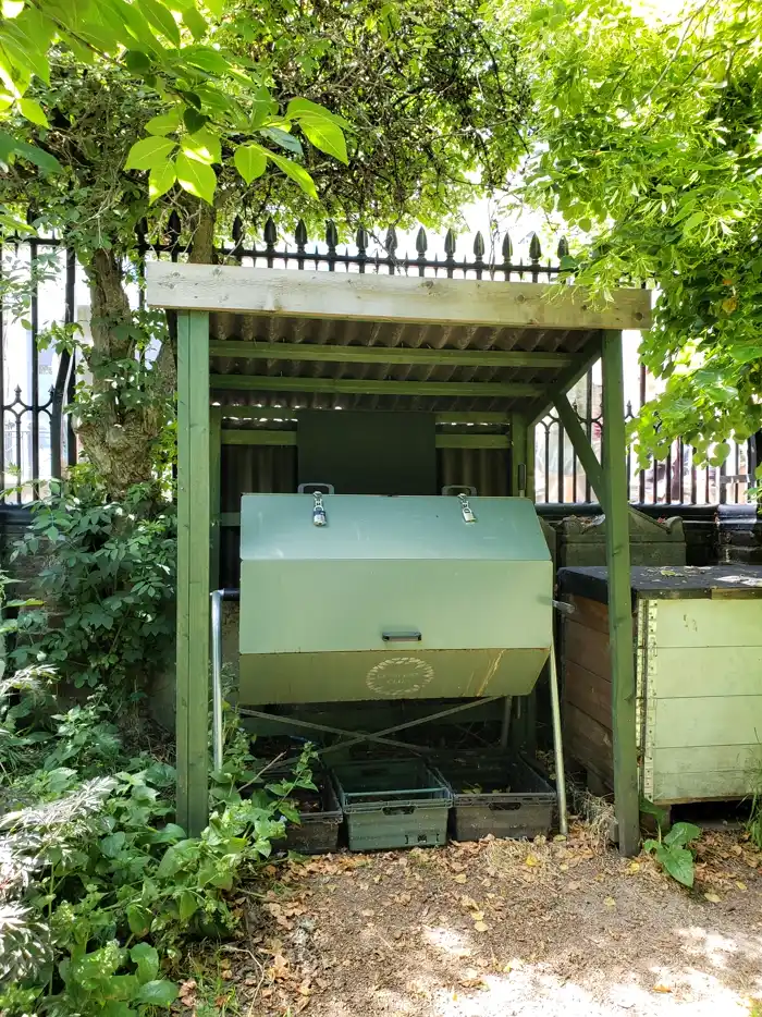 Hand-cranked rotating composter box mounted on a stand in a community garden corner