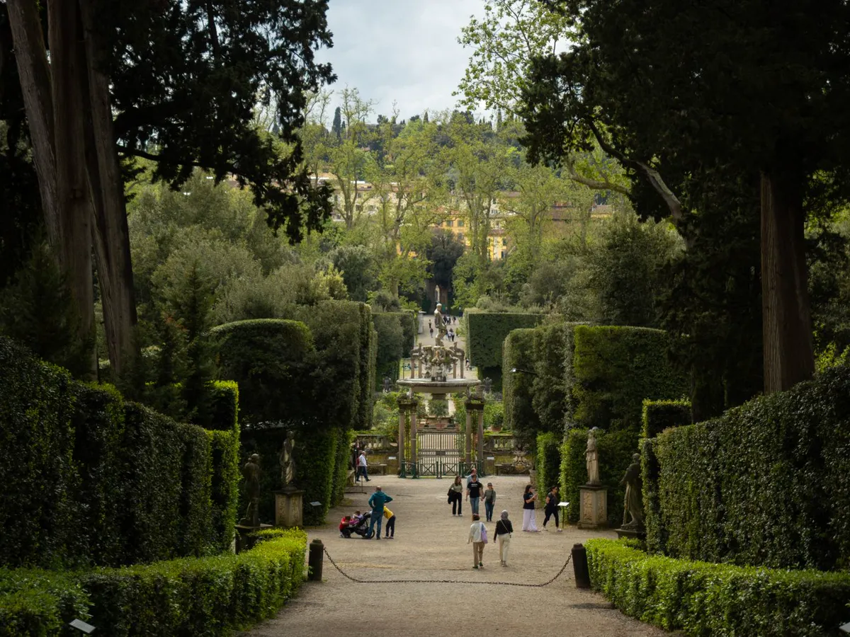 View down a cypress avenue between clipped hedges to an ornamental gate and island fountain
