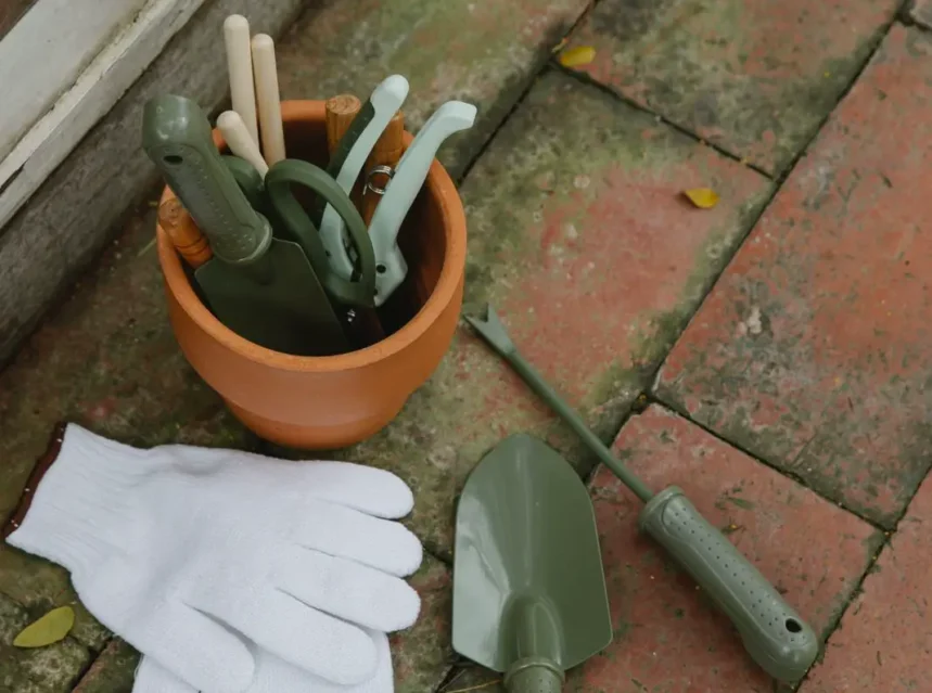 Garden tools in a terracotta pot with white gloves and a trowel on a brick path