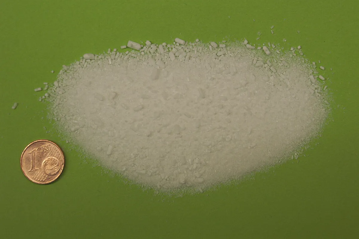 Small heap of white magnesium sulfate crystals on a green surface next to a one-cent coin for scale