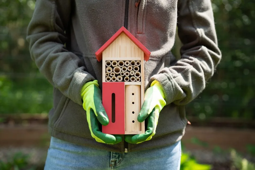 Gloved hands holding a decorative bee hotel with mixed bamboo tubes and a butterfly slit