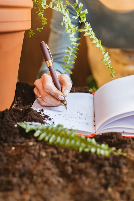 A gardener writing notes in a garden journal beside potted plants, the record My Garden keeps for you