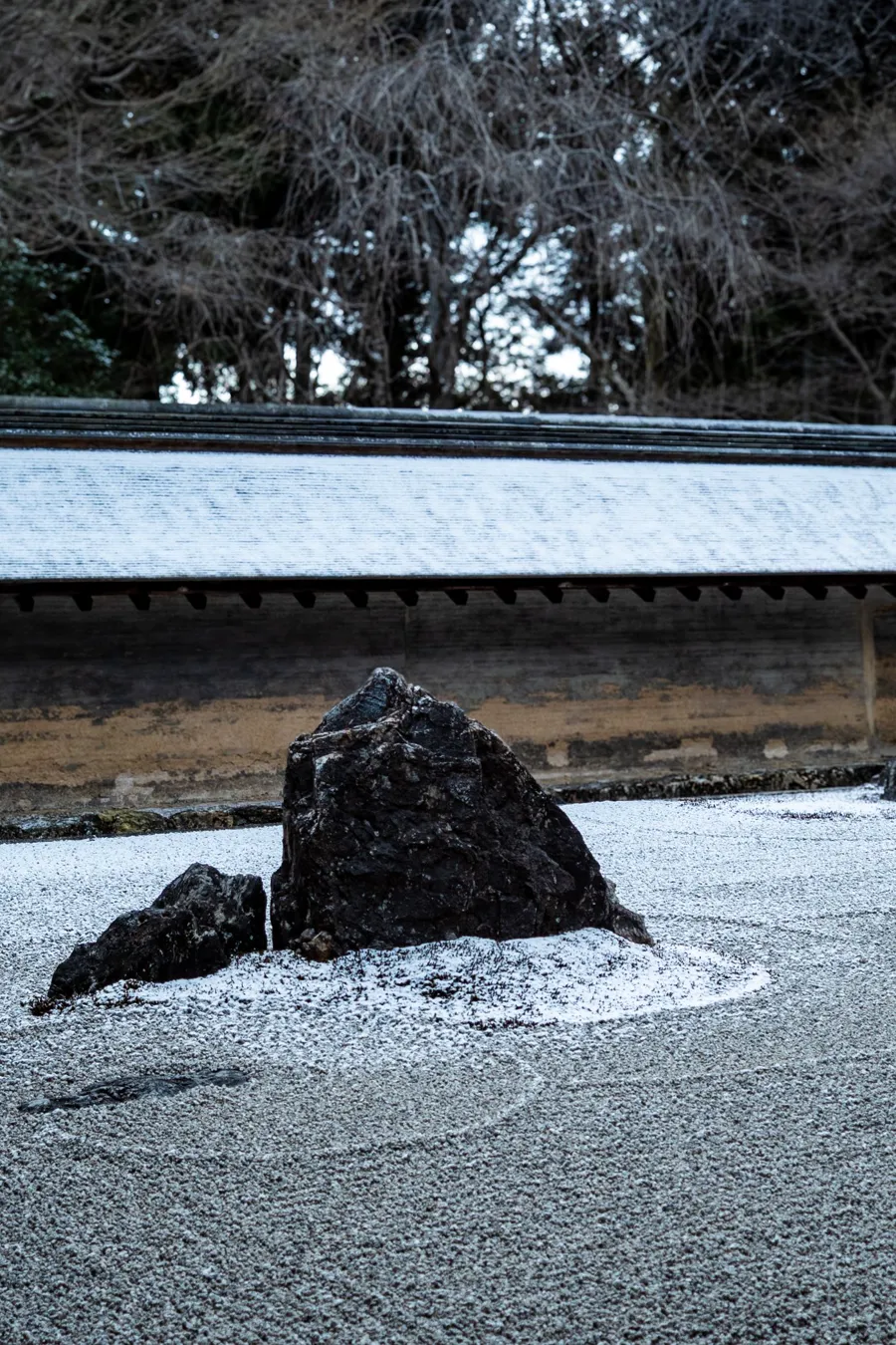 The aburadobei oil-earth wall at Ryoan-ji, its clay stained brown and ochre, behind a dark stone in the gravel