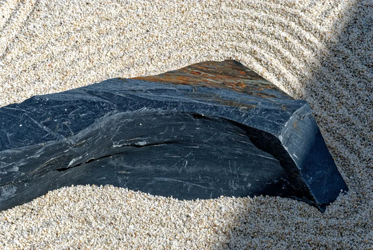 A single dark stone set into pale raked gravel, with wide empty space around it