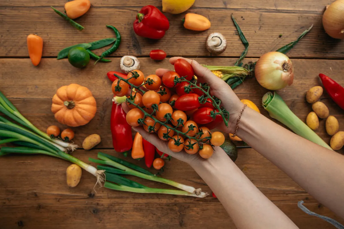 Hands holding vine tomatoes above a spread of home-grown vegetables, the range these gardening topics cover